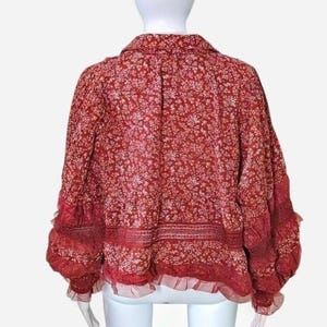 May include: A red floral print blouse with a collared neckline and long sleeves. The blouse has a ruffled hem and cuffs, and a delicate, all-over white floral pattern. The fabric appears lightweight and flowy, suitable for warmer weather.