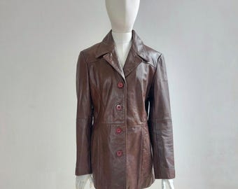 May include: A brown leather jacket with a classic design. The jacket features a collared neckline, button-up front, and long sleeves. The buttons are a darker shade of brown. The jacket is displayed on a mannequin.
