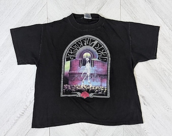 May include: Black t-shirt featuring a graphic of a skeleton in a building with the text "Grateful Dead" around the building.