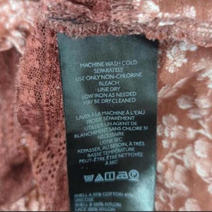 May include: A black clothing label with white text detailing washing instructions in English and French. The fabric composition includes cotton, viscose, and nylon. The background features a floral pattern in brown and white.