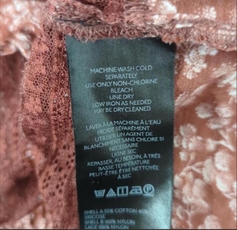 May include: A black clothing label with white text detailing washing instructions in English and French. The fabric composition includes cotton, viscose, and nylon. The background features a floral pattern in brown and white.