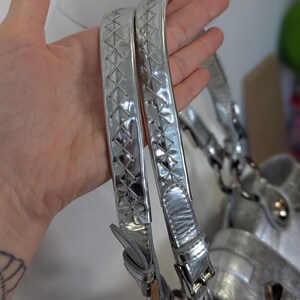 Puede incluir: Bolso de mano plateado con asas trenzadas. Las asas son de material met&aacute;lico brillante con un patr&oacute;n de diamantes. El bolso tiene un acabado plateado y herrajes met&aacute;licos.