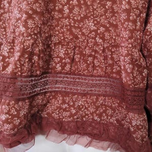 May include: A burgundy top with a floral design. It has a lace trim and a ruffled hem. The fabric appears soft and textured. The garment is likely made from a comfortable material.