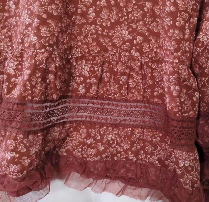 May include: A burgundy top with a floral design. It has a lace trim and a ruffled hem. The fabric appears soft and textured. The garment is likely made from a comfortable material.
