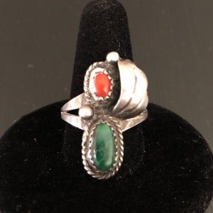 Op de afbeelding: Een zilveren ring met een groene steen en een rode steen in een draaiend ontwerp.