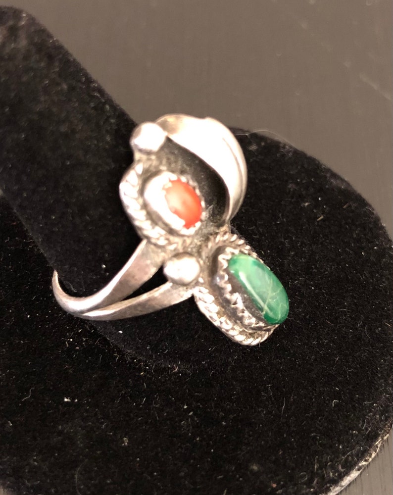 Op de afbeelding: Een zilveren ring met een groene en rode stenen setting. De ring ligt op een zwarte fluwelen achtergrond.