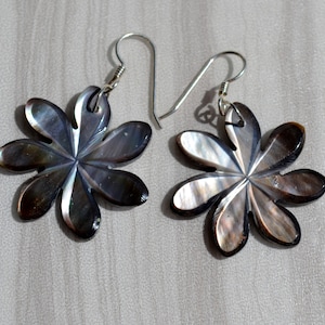 Könnte beinhalten: Ein Paar silberne Ohrringe mit einem schwarzen und schillernden Blumendesign. Die Ohrringe sind aus Perlmutt gefertigt und haben ein zartes, feminines Aussehen.