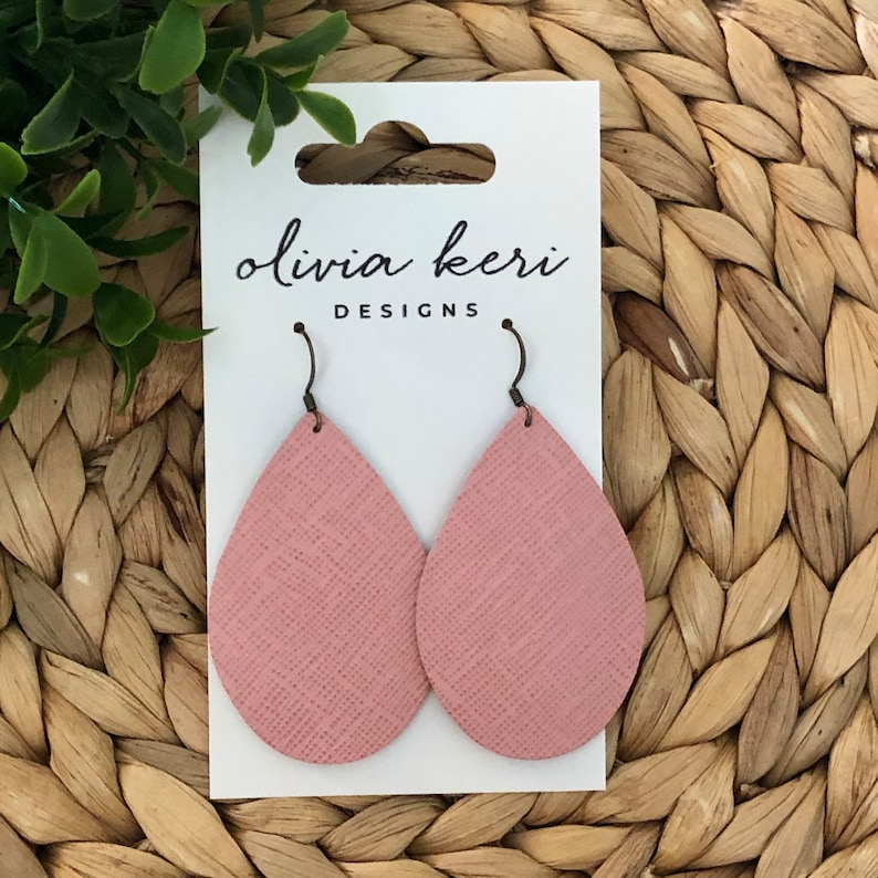 May include: A pair of pink leather teardrop earrings with a textured finish. The earrings are on a white card with the text "olivia keri DESIGNS".