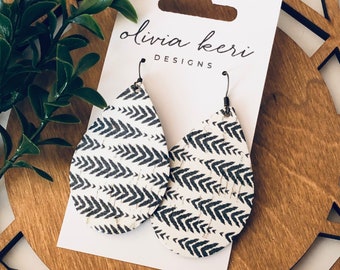 May include: A pair of white teardrop-shaped earrings with a black chevron pattern. The earrings are made of cork and have a silver hook closure. The earrings are displayed on a white card with the text "olivia kerr DESIGNS".