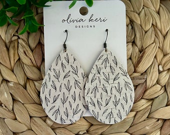 May include: A pair of teardrop-shaped cork earrings with a black and white leaf pattern. The earrings are on a white card with the text "olivia keri DESIGNS".