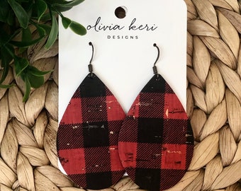 May include: A pair of teardrop-shaped earrings featuring a red and black buffalo plaid pattern on a textured cork material. The earrings hang from dark metal hooks and are displayed on a white card labeled with the text olivia keri DESIGNS.
