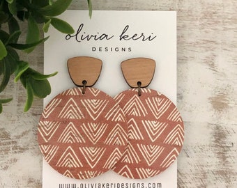 May include: A pair of wooden earrings with a geometric pattern in shades of brown and white. The earrings are round and have a wooden top piece. The earrings are on a white card with the text "olivia keri DESIGNS" and "www.oliviakeridesigns.com".