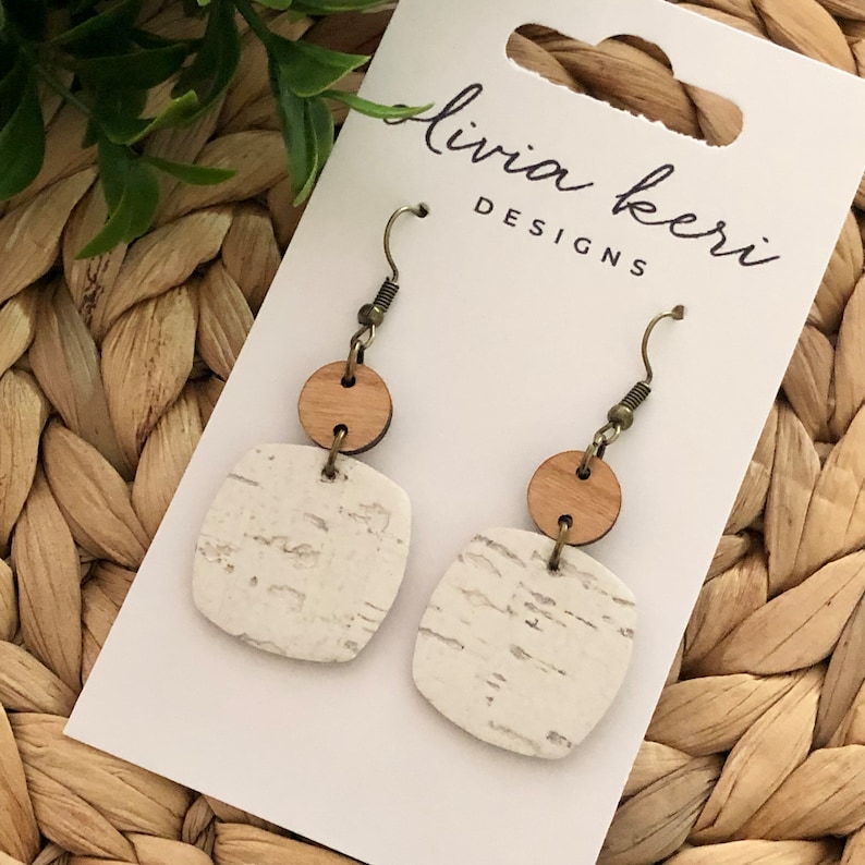 Puede incluir: Un par de pendientes de corcho blanco y marr&oacute;n con forma cuadrada y un acento redondo de madera. Los pendientes est&aacute;n en una tarjeta blanca con el texto "livia kerr designs".