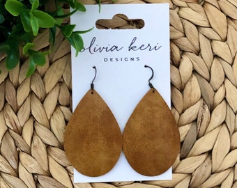 May include: A pair of brown leather teardrop earrings with silver hooks. The earrings are on a white card with the text "Olivia Keri Designs".