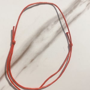 Puede incluir: Un sencillo brazalete de cuerda roja, atado con un nudo en cada extremo.