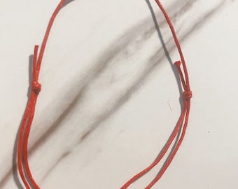 Könnte beinhalten: Ein einfaches rotes Armband aus Schnur, an beiden Enden mit einem Knoten gebunden.