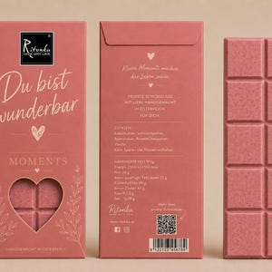 Könnte beinhalten: Eine rosa Schokoladentafel mit segmentierter Oberfläche, begleitet von der Vorder- und Rückseite der Verpackung. Die Vorderseite zeigt den Text "Du bist wunderbar" und einen herzförmigen Ausschnitt. Die Rückseite enthält Nährwertangaben.