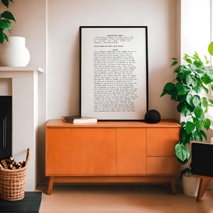 May include: A black framed print with a white background and black text. The text is a quote about the expectations of women. The print is hanging on a wall above a burnt orange cabinet.