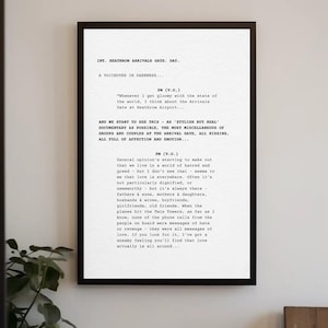 Può includere: Una stampa incorniciata con un estratto di sceneggiatura con il testo "INT. HEATHROW ARRIVALS GATE, DAY." e un monologo sull'amore. La stampa è in una cornice nera ed è appesa a un muro bianco. Una pianta è visibile.