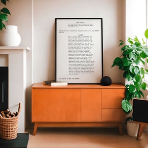 May include: A framed black and white print with a typewriter font text about fashion and style. The print is hanging on a wall above a burnt orange cabinet with a book on top. A green plant is in a white pot on the right side of the image.