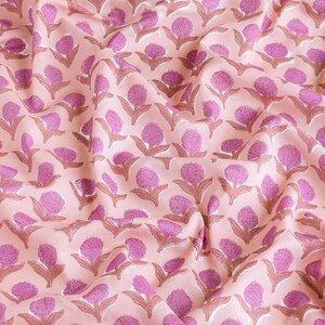 May include: Peach-coloured fabric with a repeating pattern of pink stylised flowers. The fabric is wrinkled and has a soft, natural texture.