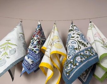 Pode incluir: Cinco panos de cozinha decorativos com vários padrões florais e botânicos pendurados numa corda. Os panos apresentam detalhes em branco, azul, amarelo e verde. Cada pano é dobrado e preso à corda, mostrando os diferentes desenhos.