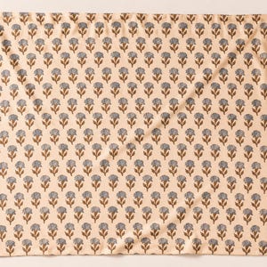 May include: A square fabric textile featuring a repeating pattern of small, stylized blue flowers with brown stems and leaves arranged in uniform rows against a light cream-colored background. The cloth has a soft, folded texture throughout.