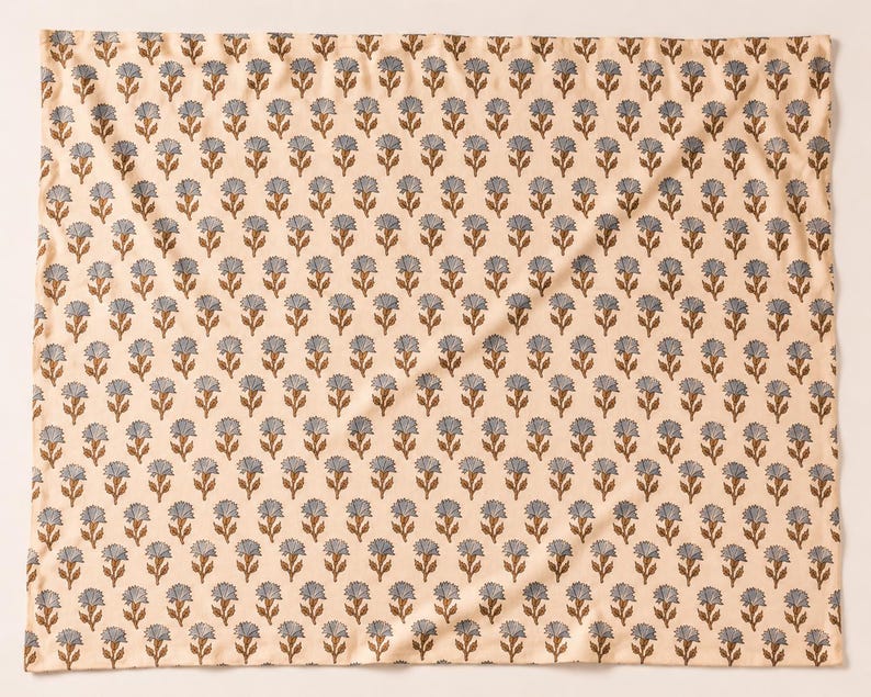 May include: A square fabric textile featuring a repeating pattern of small, stylized blue flowers with brown stems and leaves arranged in uniform rows against a light cream-colored background. The cloth has a soft, folded texture throughout.