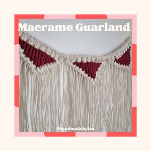 Peut inclure: Une guirlande en macramé blanche avec des formes triangulaires rouges. La guirlande a de longues franges et est suspendue à un mur blanc. Le texte "Macrame Garland" et "@handmadebylau" sont visibles sur l'image.