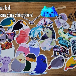 May include: A collection of colorful stickers featuring various animals, including birds, penguins, a husky, a zebra, a bear, and a cat. The stickers are on a wooden surface. The text "Take a look at some of my other stickers!" is visible in the top left corner of the image.