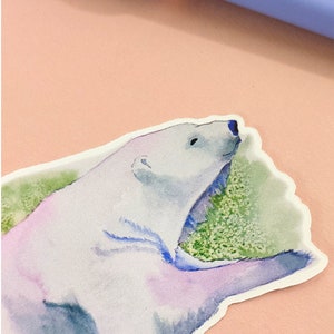 May include: A watercolor sticker of a polar bear with a light blue, purple, and green background. The bear is facing to the right and has its mouth open.