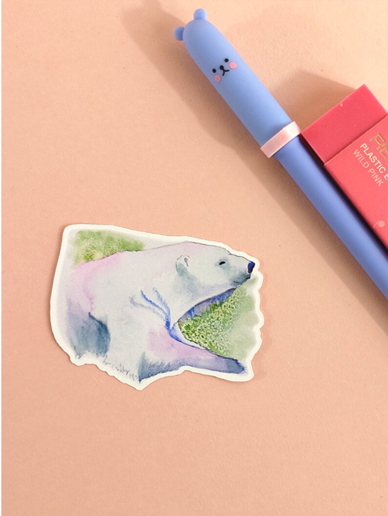 May include: A watercolor sticker of a polar bear lying down on a green background. The sticker is white with blue and purple watercolor accents.