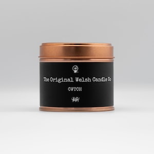 Puede incluir: Una lata de vela negra con ribete de cobre. La etiqueta dice "The Original Welsh Candle Co." y "CWTC", con un pequeño símbolo de dragón debajo del texto.