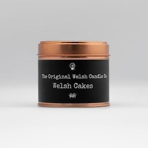 May include: A black tin candle with a copper lid. The label reads "The Original Welsh Candle Co. Welsh Cakes".