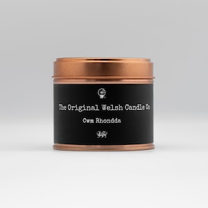 Könnte beinhalten: Eine schwarze Blechkerze mit einem kupfernen Deckel. Das Etikett lautet "The Original Welsh Candle Co. Cwm Rhondda" mit einer kleinen Drachengrafik.
