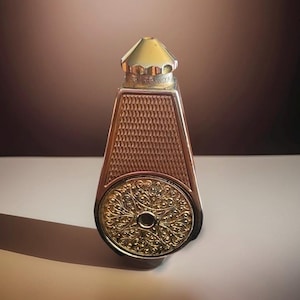 May include: A vintage perfume bottle with a gold cap and intricate detailing. The bottle features a geometric pattern on the front and a circular, decorative base. The design incorporates gold and bronze tones.