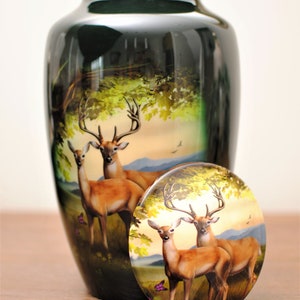 K&ouml;nnte beinhalten: Eine schwarze Keramikurne mit einer bemalten Szene von zwei Hirschen in einer Waldlandschaft. Der Deckel der Urne zeigt die gleiche Szene.