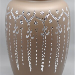 May include: A brown ceramic urn with a silver floral design. The urn has a lid and is decorated with a repeating pattern of flowers and leaves.