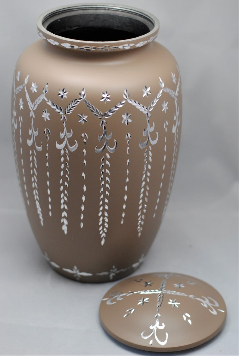 May include: A brown ceramic urn with a silver design. The urn has a lid with a similar design. The urn is decorated with a repeating pattern of stars, leaves, and swirls.