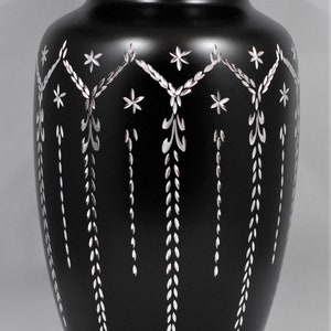 May include: Black urn with a silver floral design. The urn has a lid and is made of metal.