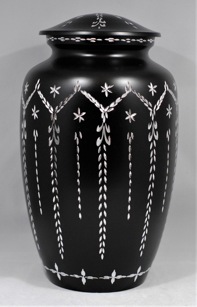 May include: Black urn with a silver floral design. The urn has a lid and is made of metal.