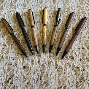 May include: Seven wooden pens with black metal accents. The pens are arranged in a row on a white lace tablecloth.