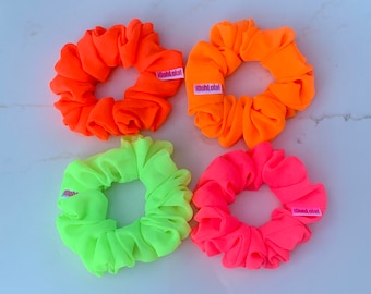 Könnte beinhalten: Vier neonfarbene Haargummis mit dem Markennamen "100%total" auf jedem. Die Haargummis sind in Orange, Grün, Pink und Gelb.