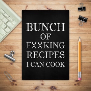 以下が含まれることがあります： 「BUNCH OF FXXKING RECIPES I CAN COOK」と白字で書かれた黒板スタイルの看板。キーボード、鉛筆、ペーパークリップ、バインダークリップが置かれた木製の表面に看板があります。