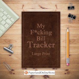 May include: A brown leather-bound journal with the title "My F*cking Bill Tracker" in large print. The journal is on a wooden surface with a pencil, paper clips, and a keyboard.
