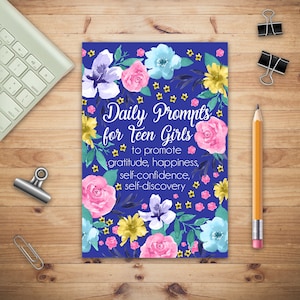 May include: A blue background with watercolour flowers in pink, yellow, blue, and purple. The text "Daily Prompts for Teen Girls" is in white with a black outline. The text "to promote gratitude, happiness, self-confidence, self-discovery" is in white.