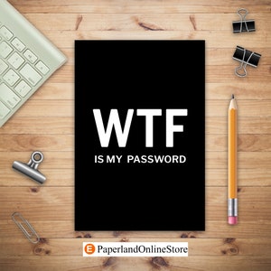 May include: Black and white notebook with the text "WTF IS MY PASSWORD" in white letters. The notebook is on a wooden surface with a pencil, paper clips, and a keyboard.