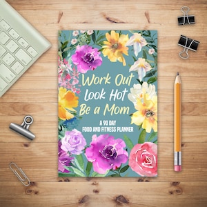 Puede incluir: Un planificador azul con un diseño floral y el texto "Work Out Look Hot Be a Mom A 90 Day Food and Fitness Planner".