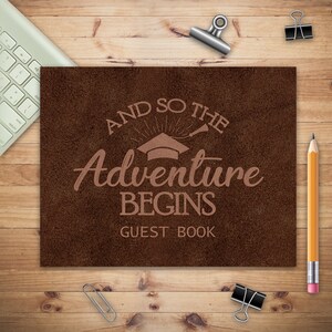 May include: Brown leather guest book with the text "And so the adventure begins" and a graduation cap graphic.