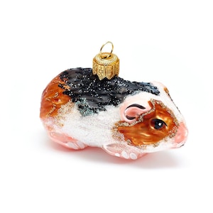 Puede incluir: Un adorno de Navidad de vidrio con forma de conejillo de indias. El conejillo de indias es marrón, blanco y negro con un acabado brillante. Tiene un colgador de adorno dorado.
